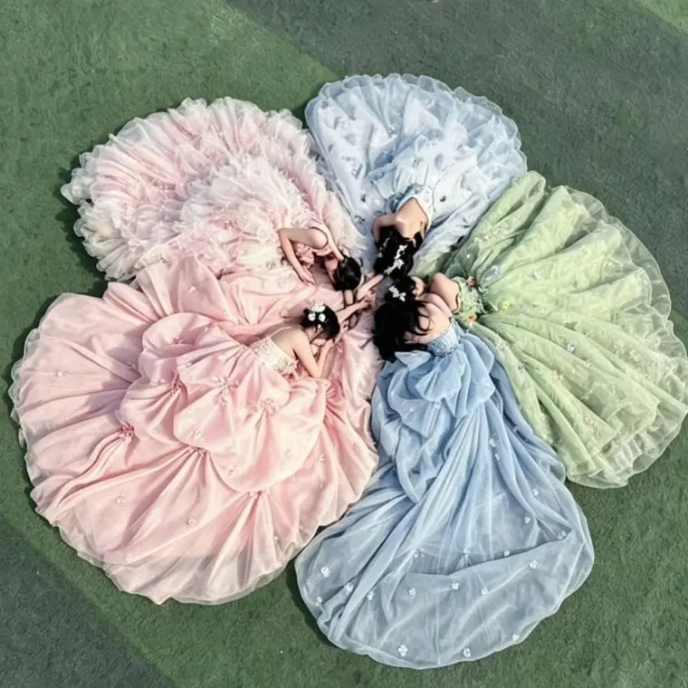 Four ball gowns fanned into a flower shape, shot from above on green turf.