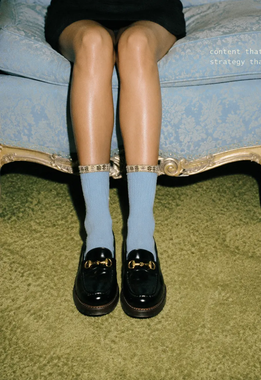 Legs in blue socks and black loafers on a blue settee, captioned content that plays, strategy that wins.