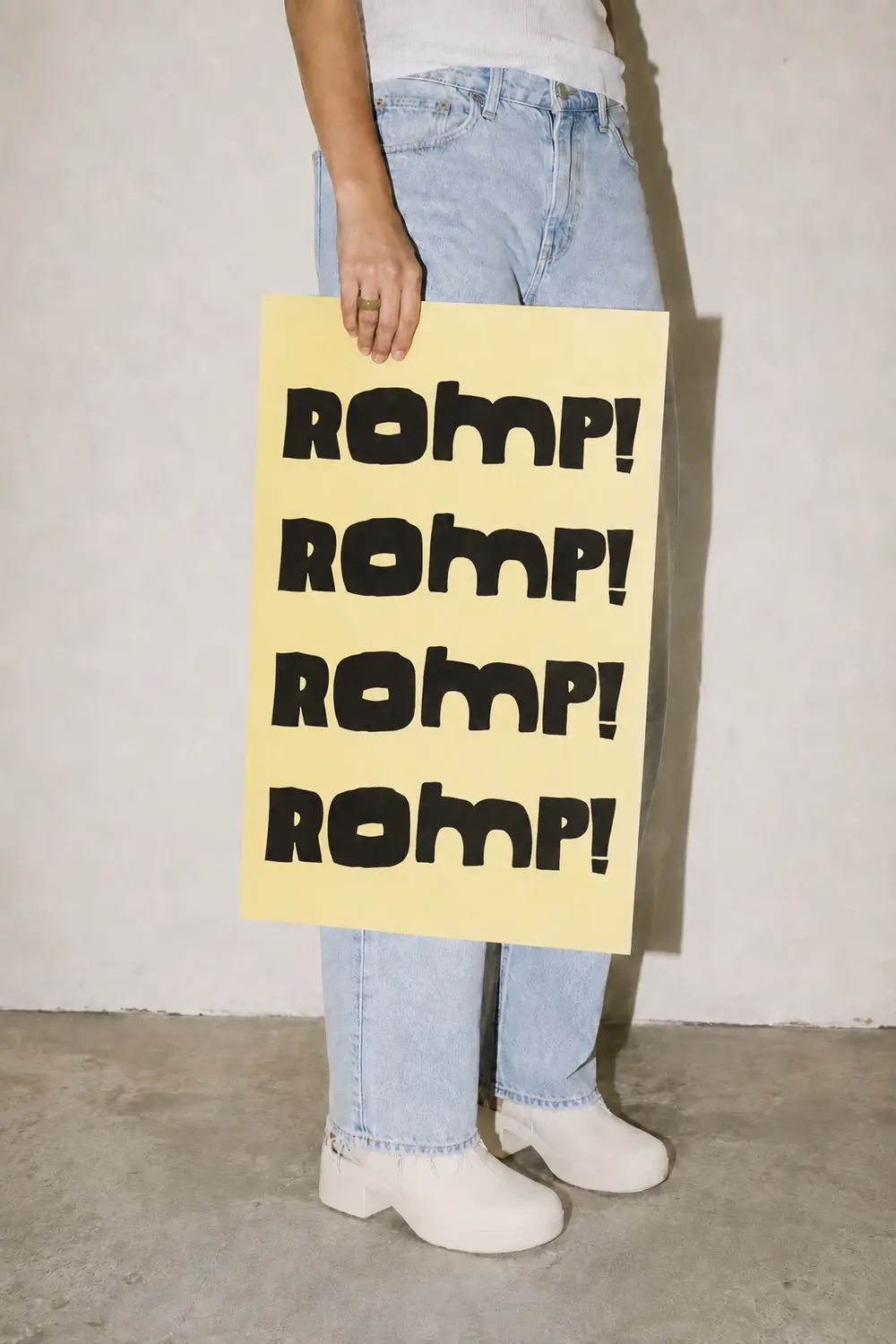 Someone holding a yellow poster printed with the ROMP wordmark four times.